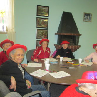 Group of senior ladies wearing red hats coloring at the table